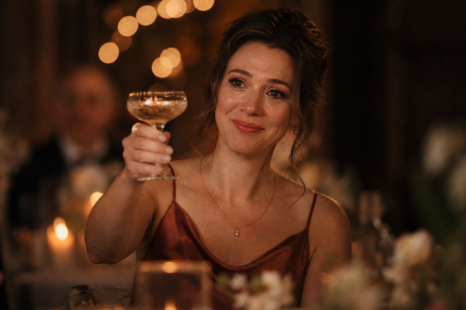 Wedding guest mid-toast, holding a coupe of champagne in candlelight